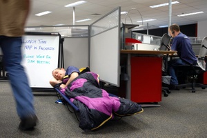 someone napping in a sleeping bag in a work cubicle